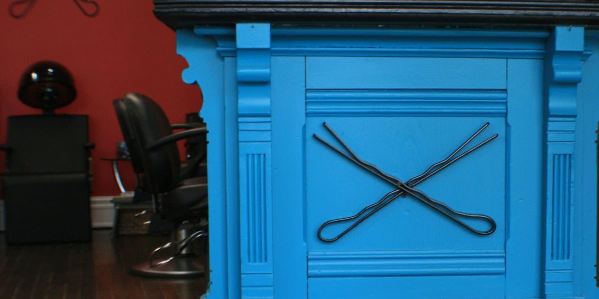 The Hair Pin's reception desk with a crossed hair pin detail against a red salon wall