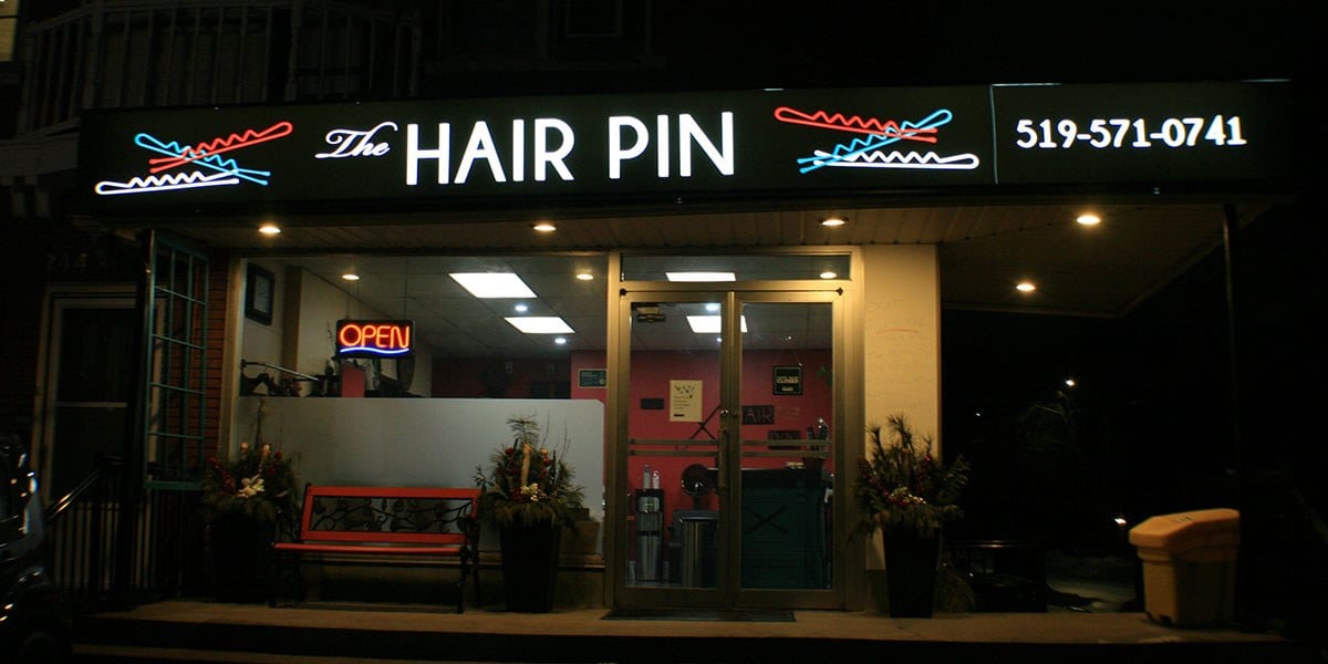 The lit storefront sign for The Hair Pin at night on Queen Street in Kitchener
